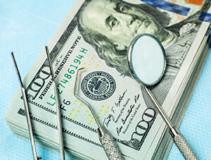 Money and dental tools representing cost of dental implants in Friendswood
