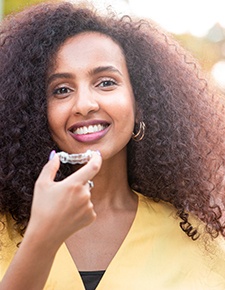 Woman with yellow shirt putting in Invisalign in Friendswood, TX