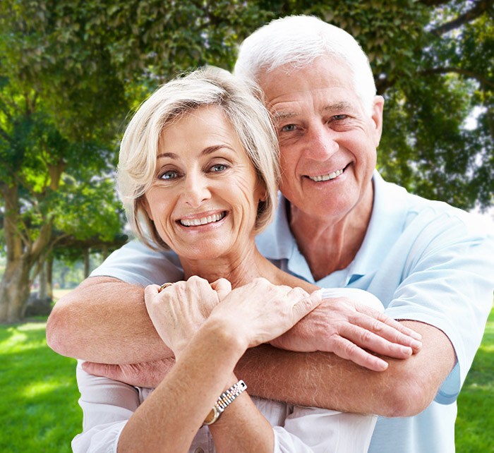 Older couple smiling and hugging after tooth replacement with dental implants