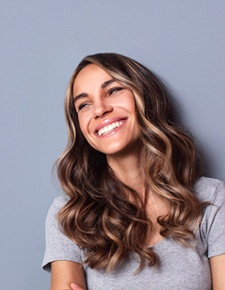 Woman in gray t-shirt with beautiful, confident smile after cosmetic dentistry