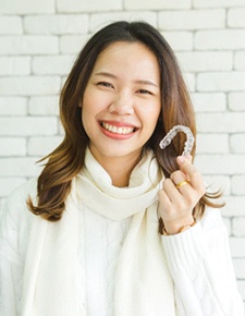 Happy woman in white sweater holding Invisalign aligner