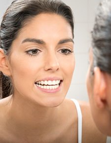 Woman looking at smile in mirror after teeth whitening