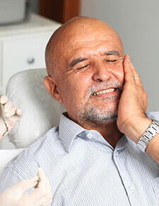 Man in dental chair holding cheek in pain before emergency dentistry