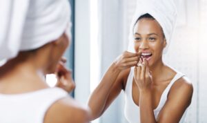 Woman in white bathrobe flossing teeth at mirror