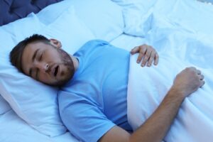 Man asleep in bed with mouth hanging open.